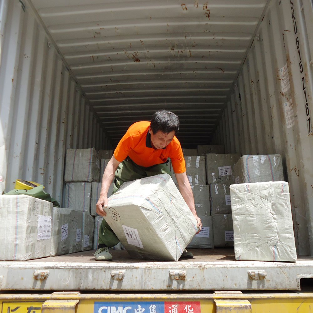 Worker handling wrapped cargo at a shipping container